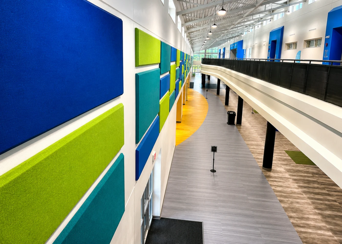 Blue, green, and teal acoustic wall panels lining a long upper-level hallway at North River Middle School